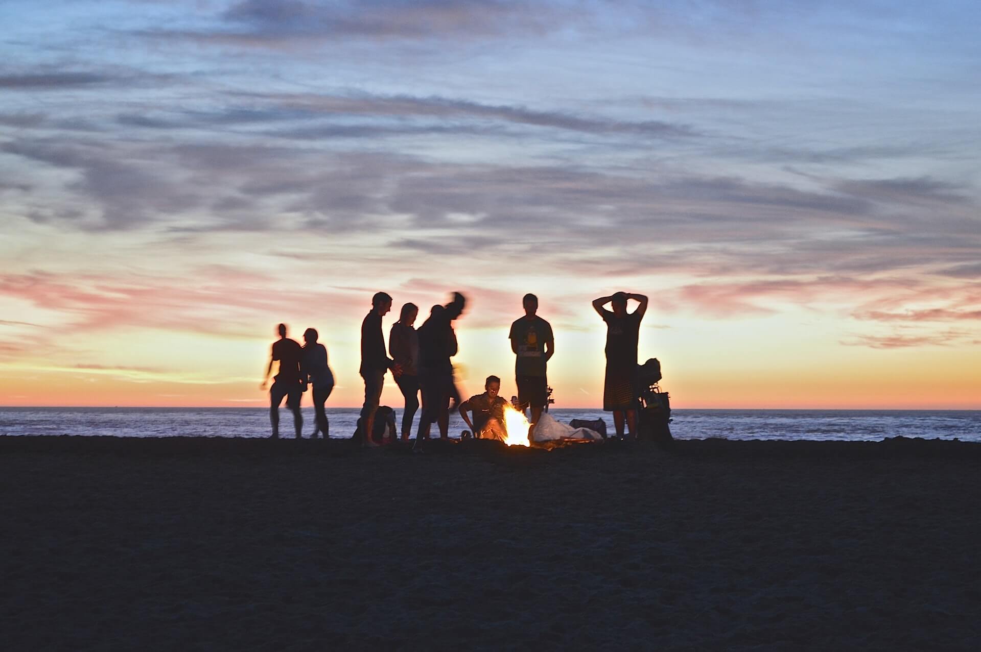 A group of people having a fire on a beach at sunset.