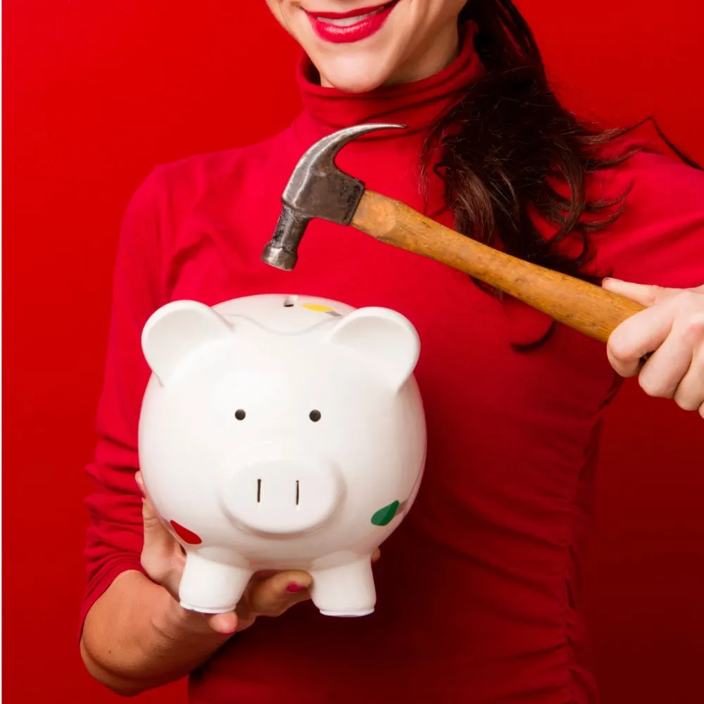 A woman about to smash a piggy bank open with a hammer