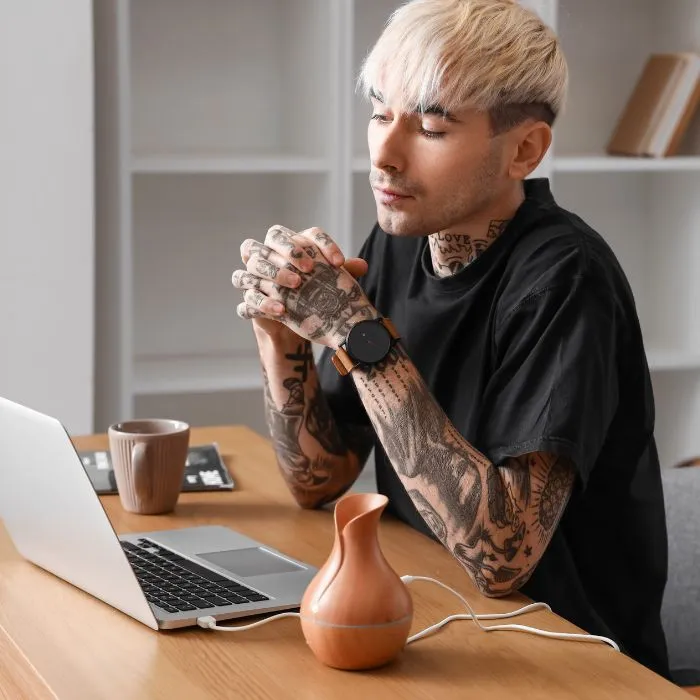 A blonde haired man with lots of tattoos watching a video on his laptop.